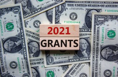 Symbol of planning 2021. Wooden blocks with words '2021 Grants'. Beautiful background from dollar bills, copy space. Business and 2021 grants concept.
