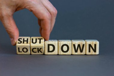 Lockdown or shutdown. Male hand flips wooden cubes and changes the word 'lockdown' to 'shutdown'. Beautiful grey background, copy space. Business and lockdown or shutdown concept.