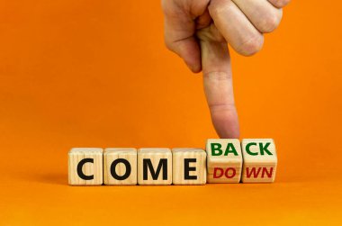 Comedown or comeback symbol. Male hand flips wooden cubes and changes the word 'comedown' to 'comeback'. Beautiful orange background, copy space. Business and comeback concept.