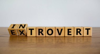 Introvert or extrovert symbol. Fliped cubes and changed the word 'introvert' to 'extrovert'. Beautiful wooden table, white background, copy space. Psychological and Introvert or extrovert concept. clipart