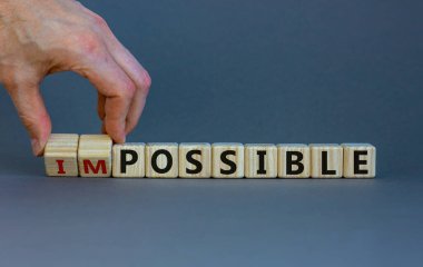 Possible or impossible. Male hand flips wooden cubes and changes the word 'impossible' to 'possible'. Beautiful grey background, copy space. Business and possibility concept.