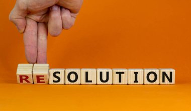 New years solution or resolution. Male hand flips wooden cubes and changes words 'solution' to 'resolution'. Beautiful orange background, copy space. Business and new years resolution concept.