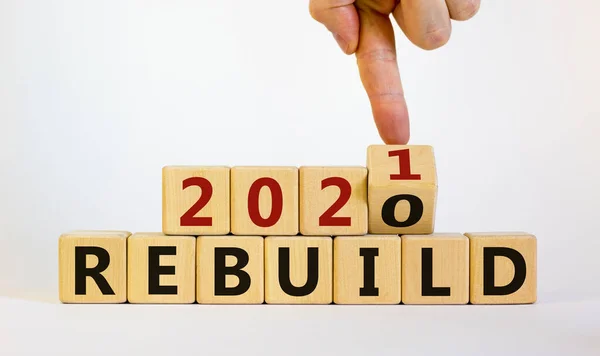 Symbol of 2021 rebuild. Male hand flips wooden cubes and changes the inscription \'Rebuild 2020\' to \'Rebuild 2021\'. Beautiful white background, copy space. Business and 2021 rebuild concept.