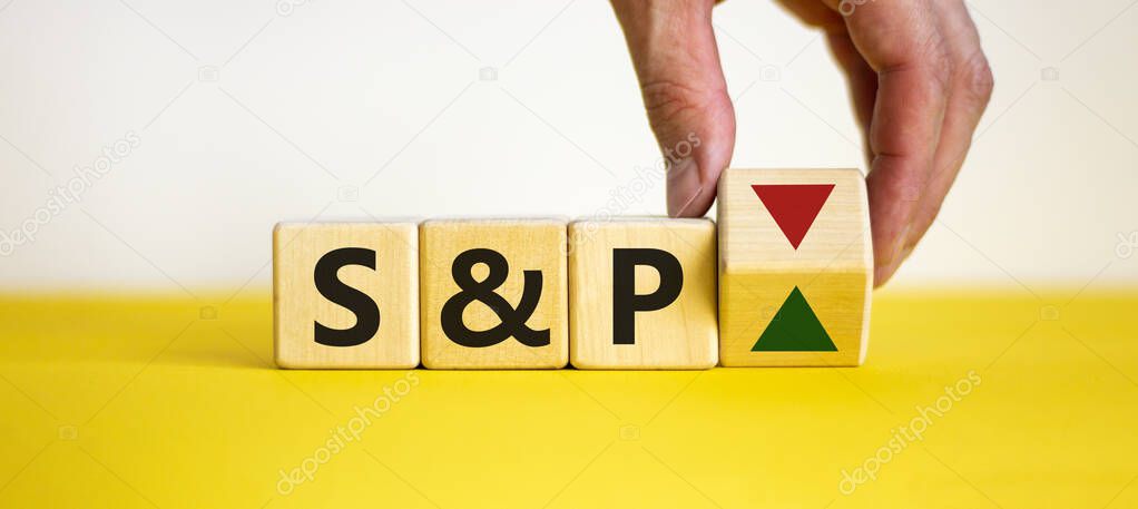Hand is turning a dice and changes the direction of an arrow symbolizing that the S&P500 Index is changing the trend and goes up instead of down. Business and S&P concept.