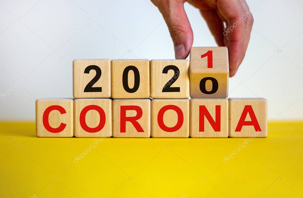 Covid-19 pandemic in 2021 symbol. Male hand flips a wooden cube and changes words 'corona 2020' to 'corona 2021'. Beautiful yellow table, white background, copy space. 2021 corona concept.