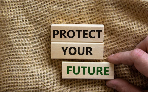 Protect your future symbol. Wooden blocks with words \'Protect your future\'. Beautiful canvas background, male hand. Copy space. Business and protect your future concept.