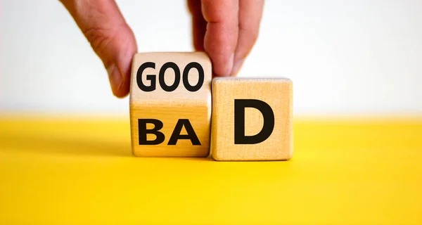 Good or bad symbol. Businessman hand turns a cube and changes the word \'bad\' to \'good\'. Beautiful yellow table, white background, copy space. Business and bad or good concept.