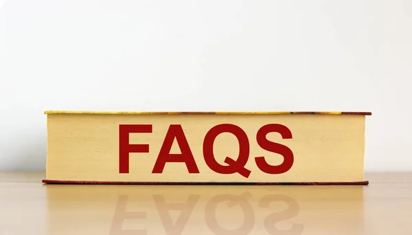 FAQS, frequently asked questions symbol. Book with word \'FAQS, frequently asked questions\' on beautiful wooden table, white background. Business and FAQS concept. Copy space.