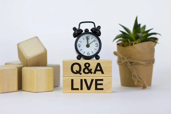 Q and A, questions and answers live symbol. Concept words \'Q and A live\' on wooden blocks on a beautiful white background. Black alarm clock and house plant. Business and Q and A live concept.