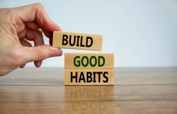 Build good habits symbol. Wooden blocks with words \'build good habits\'. Male hand. Beautiful wooden table, white background, copy space. Business, psychological and build good habits concept.