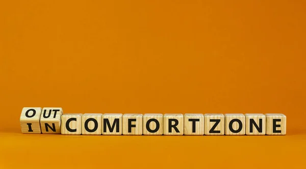 Out or in comfort zone symbol. Turned wooden cubes and changed words 'in comfort zone' to 'out comfort zone'. Beautiful orange background, copy space. Business, psychology concept.