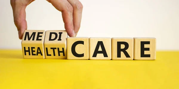 Medicare or healthcare symbol. Doctor turns cubes, changes the word 'healthcare' to 'medicare'. Beautiful yellow table, white background. Copy space. Medical, medicare or healthcare concept.