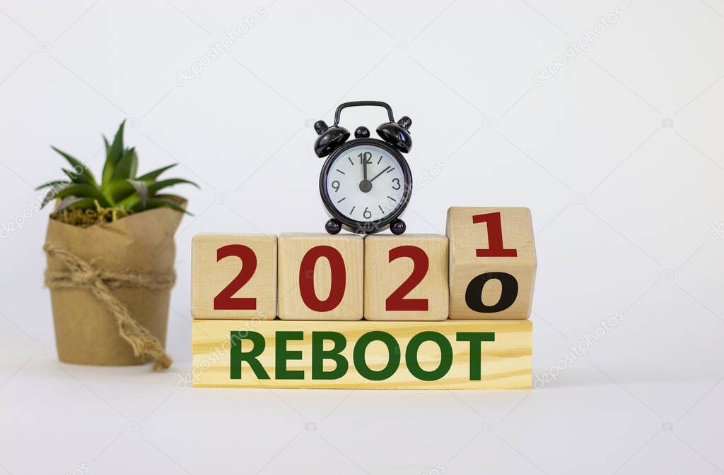 Business and 2021 new year reboot symbol. Fliped wooden cube and changed words 'reboot 2020' to 'reboot 2021'. Alarm clock, plant. Beautiful white background, copy space. Business reboot concept.