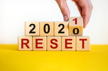 2021 'in sembolü sıfırlandı. İşadamı ahşap küpleri çeviriyor ve '2020' yi sıfırla 'yı' 2021 'e sıfırla' olarak değiştiriyor. Güzel sarı ve beyaz arka plan, kopyalama alanı. İş ve 2021 yeni yıl konseptini sıfırladı.