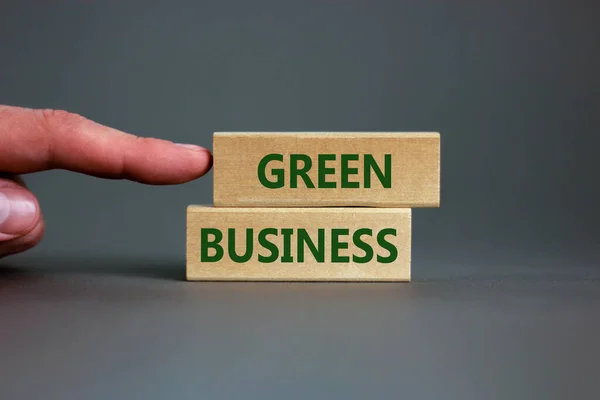 Green business symbol. Wooden blocks form the words \'green business\' on beautiful grey background. Businessman hand. Business, ecological and green business concept. Copy space.