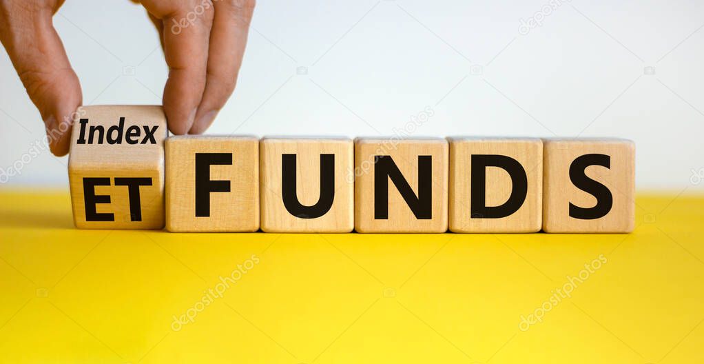 Index funds vs ETF symbol. Businessman turns a cube and changes words 'ETF' to 'Index funds. Beautiful yellow table, white background, copy space. Business and ETF and index funds concept.