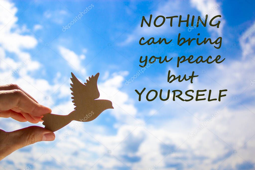 Man hand holding wooden bird on cloud sky background. Words 'nothing can bring you peace but yourself'. The development of the imagination, copy space. Motivational and business concept.