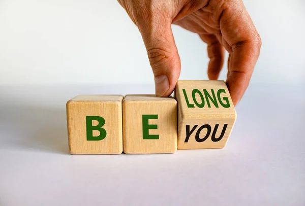 Be you, belong symbol. Businessman hand turns a cube and changes words \'be you\' to \'belong\'. Beautiful white background. Business, belonging and be you, belong concept. Copy space.