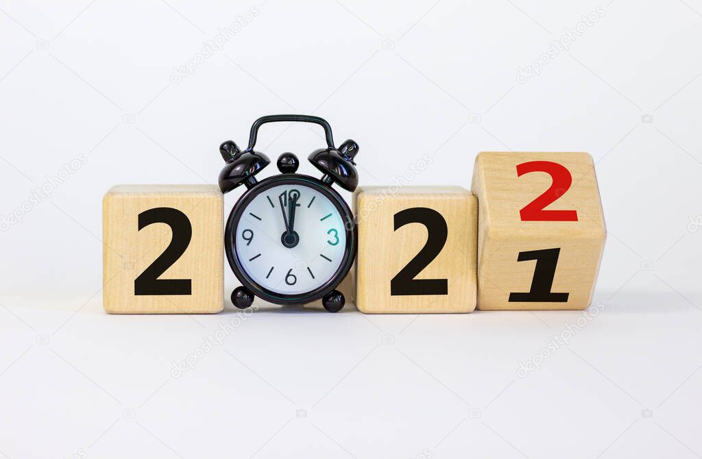 Business concept of 2022 new year. Turned a wooden cube and changed number 2021 to 2022. Black alarm clock. Beautiful white background, copy space. 2022 new year concept.