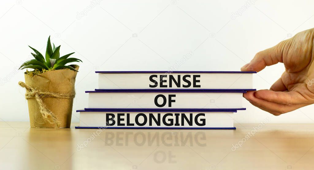 Sense of belonging symbol. Books with words 'sense of belonging' on beautiful white background. Businessman hand. Business, sense of belonging concept. Copy space.