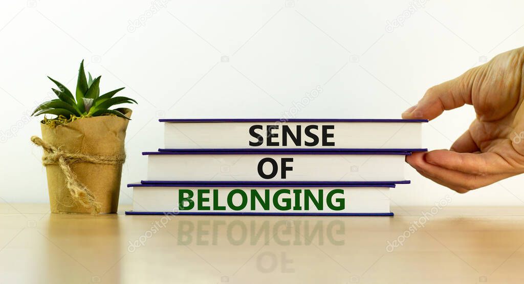 Sense of belonging symbol. Books with words 'sense of belonging' on beautiful white background. Businessman hand. Business, sense of belonging concept. Copy space.