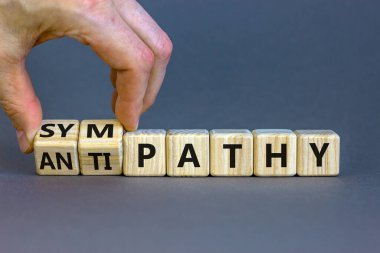 From antipathy to sympathy. Businessman turns cubes and changes the word 'antipathy' to 'sympathy'. Beautiful grey background. Copy space. Psychological and antipathy or sympathy concept. clipart