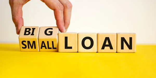 Big or small loan symbol. Businessman turns a wooden cube and changes words 'small loan' to 'big loan'. Beautiful yellow table, white background, copy space. Business and big or small loan concept.