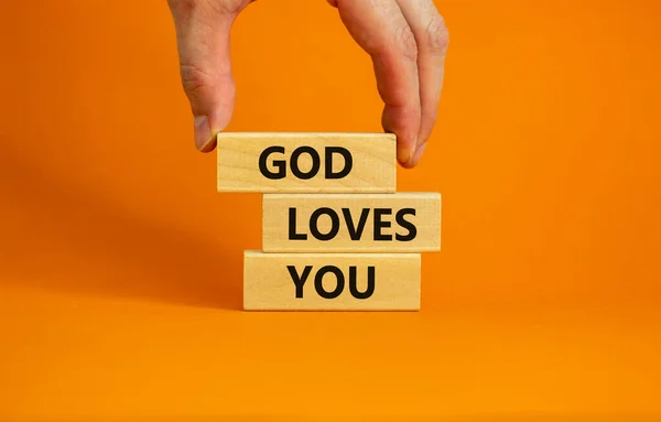 God loves you symbol. Concept words \'God loves you\' on wooden blocks on a beautiful orange background, prayer hand. Copy space. Religion and God loves you concept.