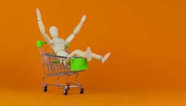 Satış zamanı sembolü. Alışveriş arabasındaki ahşap bir insan modeli. Güzel turuncu arka plan. İş ve satış kavramı, kopyalama alanı.