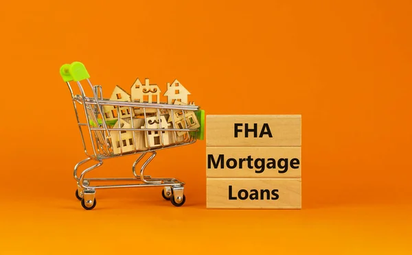 FHA mortgage loans symbol. Wooden blocks with words 'FHA mortgage loans' on beautiful orange background. Shopping cart with miniature wooden houses. Business, FHA mortgage loans concept. Copy space.