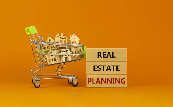 Real estate planning symbol. Wooden blocks, words \'Real estate planning\' on beautiful orange background. Shopping cart, miniature wooden houses. Business, Real estate planning concept. Copy space.