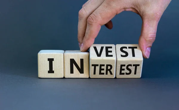 Invest or interest symbol. Businessman turns wooden cubes and changes the word 'invest' to 'interest'. Beautiful grey background, copy space. Business and invest or interest concept.