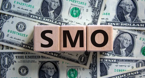 SMO, social media optimization symbol. Wooden cubes with word \'SMO, social media optimization\' on beautiful background from dollar bills, copy space. Business, SMO - social media optimization concept.