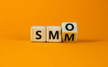 SMM, SMO sembolüne karşı. Küpü çevirdi ve 'SMM, sosyal medya pazarlaması' nı 'SMO, sosyal medya optimizasyonu' na çevirdi. İş, SMM ve SMO konsepti. Güzel turuncu arkaplan, kopyalama alanı.