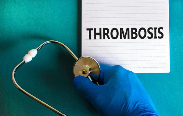 Medical and thrombosis symbol. Doctor hand, stethoscope. White note with the word 'thrombosis'. Beautiful blue background. Doctor hand in blue glove. Medical and and thrombosis concept. Copy space.