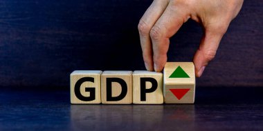 GDP, gross domestic product symbol. Businessman holds a cube with up and down icon. Word 'GDP'. Beautiful grey background. Copy space. Business and growth of GDP, gross domestic product concept.