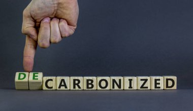 Carbonized or decarbonized symbol. Businessman turns wooden cubes and changes words 'carbonized' to 'decarbonized'. Grey background, copy space. Business, Carbonized or decarbonized concept. clipart