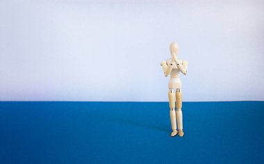 Prayer symbol. Wooden model of a human. Space for your inscription. Copy space. Beautiful blue table, white background. Religion, prayer concept.