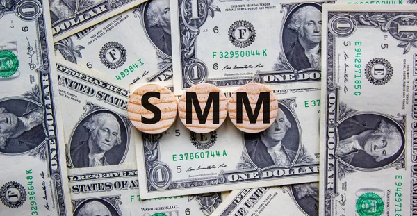 SMM, social media marketing symbol. Wooden circles with word \'SMM - social media marketing\' on beautiful background from dollar bills, copy space. Business, SMM - social media marketing concept.
