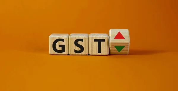 GST, goods and services tax symbol. Wooden cubes with up and down icon. Word \'GST\'. Beautiful orange background. Copy space. Business and growth of GST, goods and services tax concept.