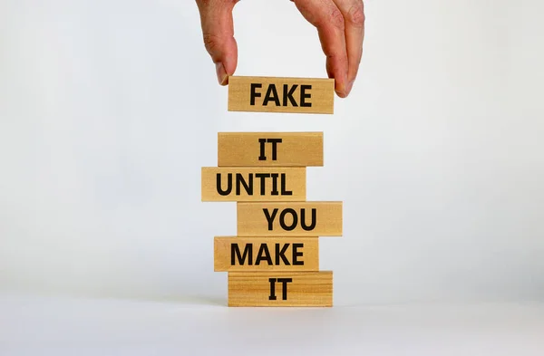 Fake it until you make it symbol. Wooden blocks with words 'Fake it until you make it'. Businessman hand. Beautiful white background. Business, popular quotation concept. Copy space.