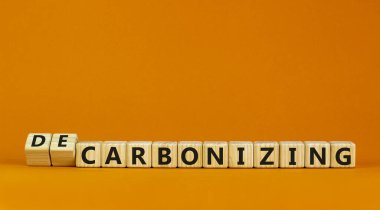 Carbonizing or decarbonizing symbol. Turned wooden cubes and changed words 'carbonizing' to 'decarbonizing'. Orange background, copy space. Business, carbonizing or decarbonizing concept. clipart