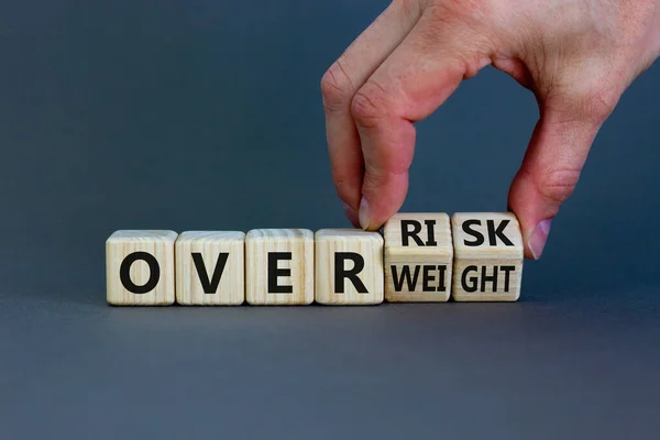 High risk from overweight symbol. Doctor turns wooden cubes and changes the words overweight to over risk. Beautiful grey background, copy space. Medical and high risk from overweight concept.