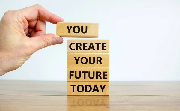 You create your future today symbol. Concept words \'You create your future today\' on wooden blocks on a beautiful white background. Businessman hand. Business, motivational and create future concept.