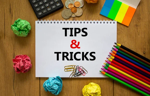 Tips and tricks symbol. White note with words \'Tips and tricks\' on beautiful wooden table, colored paper, colored pencils, paper clips, coins and calculator. Business and tips and tricks concept.