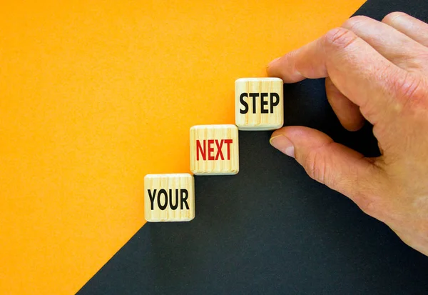 Your next step symbol. Hand arranging wood block stacking as step stair on top with words Your next Step. Business concept for personal ladder of success process. Orange background, copy space.