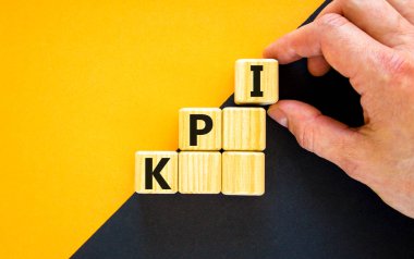 KPI, key performance indicator symbol. Wood cubes with words 'KPI, key performance indicator' on yellow background, copy space. Businessman hand. Business and KPI, key performance indicator concept.