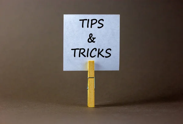 Tips and tricks symbol. White paper on wooden clothespin. Words 'Tips and tricks'. Beautiful grey background. Business and tips and tricks concept, copy space.
