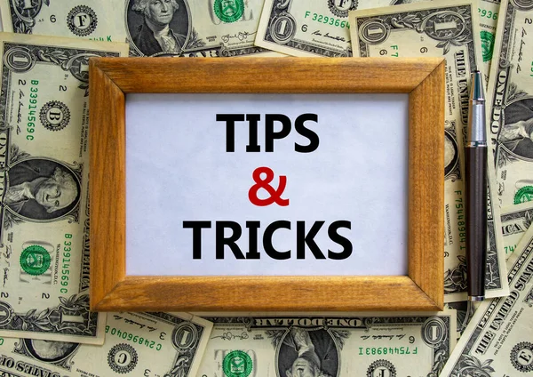 Tips and tricks symbol. Wooden frame with words 'Tips and tricks' on beautiful background from dollar bills, black pen. Business and tips and tricks concept.