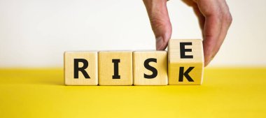 Risk yükselme sembolüne karşı. İşadamı tahta küpü dönüştürür ve yükselmek için risk kelimesini değiştirir. Güzel sarı masa, beyaz arka plan, kopyalama alanı. İş, risk ve yükseliş kavramı.